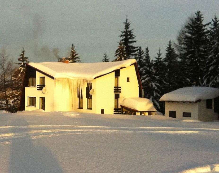 Chata Na Skalce v zimním podvečeru, zlaté světlo na sněhu, z komína stoupá kouř