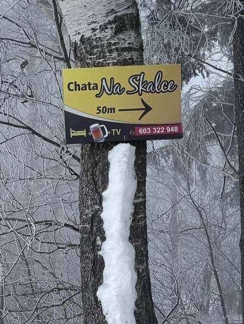 Žlutá cedule „Chata Na Skalce 50 m“ na bříze u zasněžené silnice